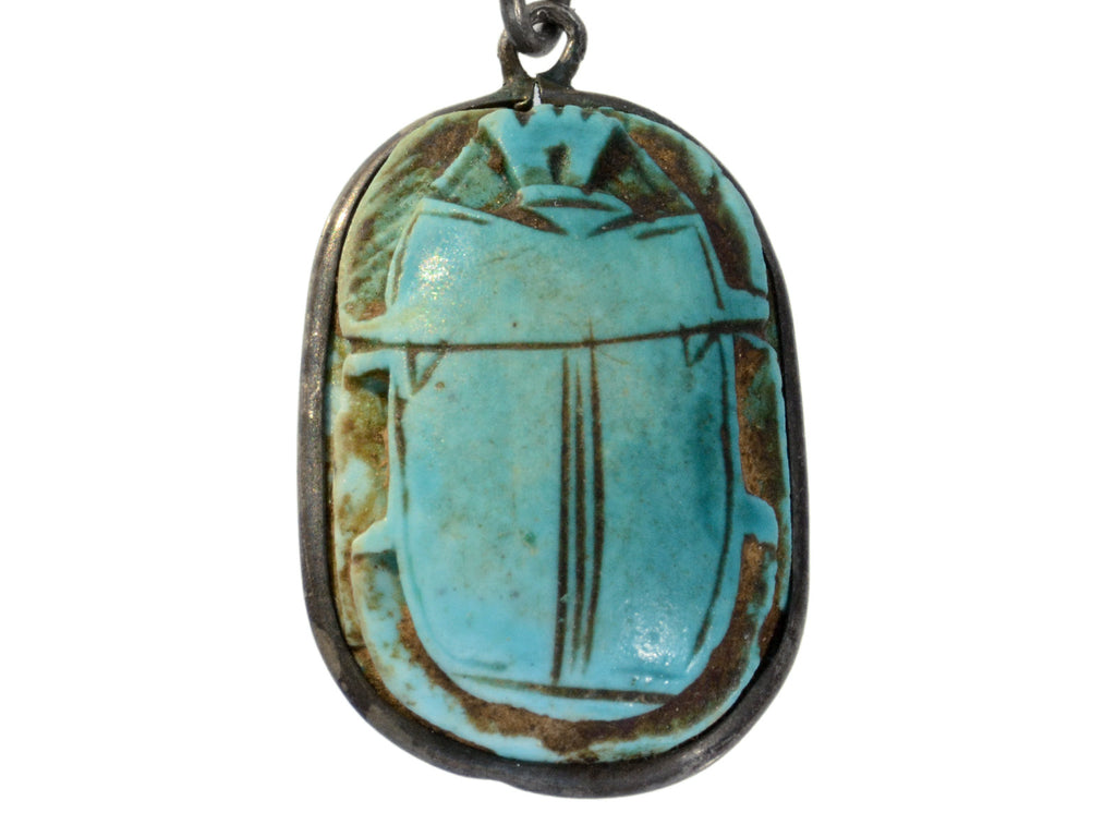 Detail of turquoise colored scarab set in silver, shown on white background.