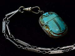 thumbnail of Detail of turquoise colored scarab and Art Deco detailed chain, shown on dark background