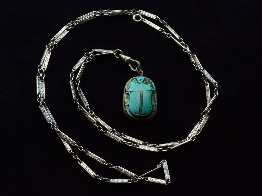 Art Deco silver necklace shown spiraled with turquoise colored scarab pendant at center.
