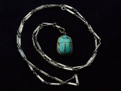 thumbnail of Art Deco silver necklace shown spiraled with turquoise colored scarab pendant at center.