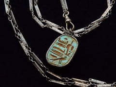 thumbnail of Detail of reverse side of scarab pendant shown faux Egyptian hieroglyphs. On dark background.