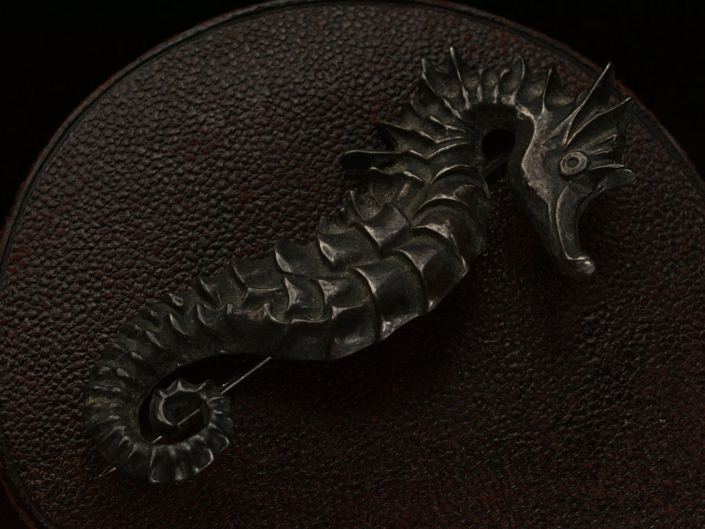 Angled view of c1970 Darkened Silver Seahorse Brooch on dark textured background.