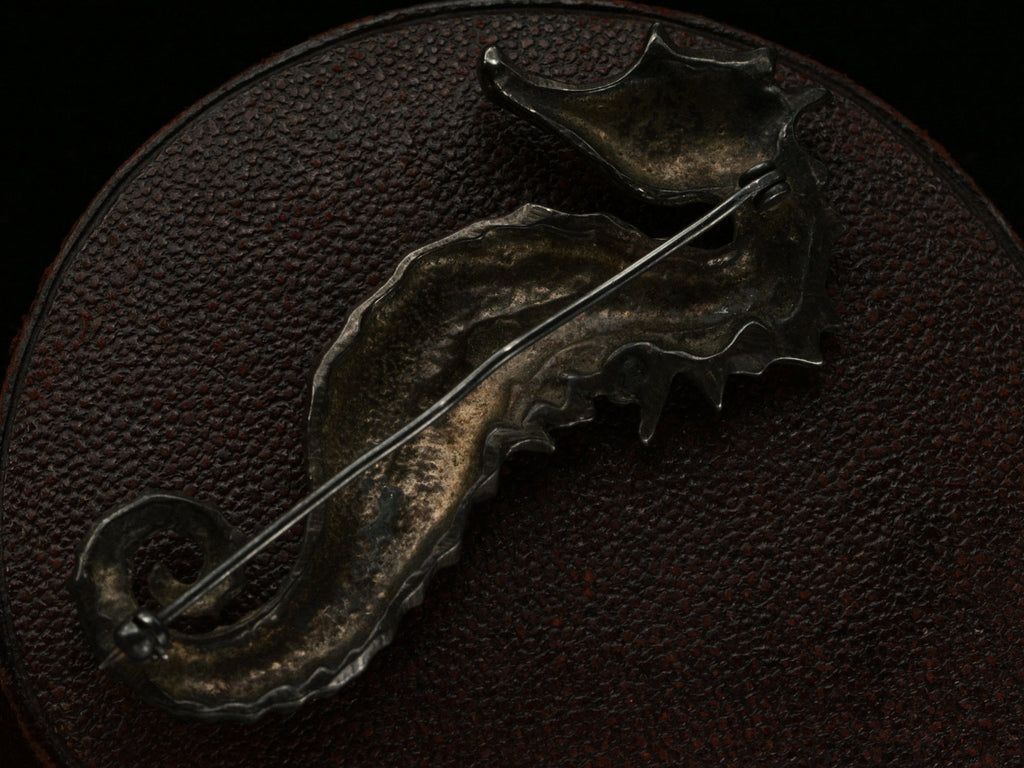 Reverse side view of c1970 Darkened Silver Seahorse Brooch on dark textured background.