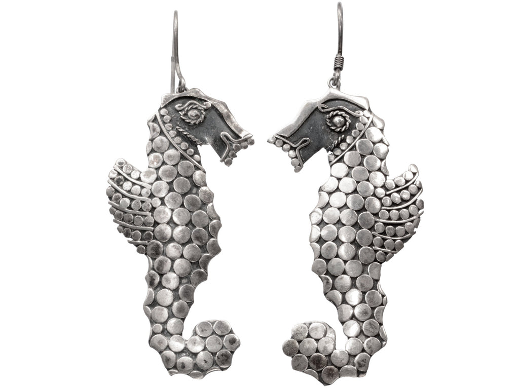 A pair of silver seahorse drop earrings textured with disks, shown against a plain white background.