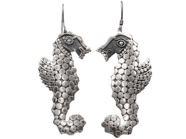 A pair of silver seahorse drop earrings textured with disks, shown against a plain white background.