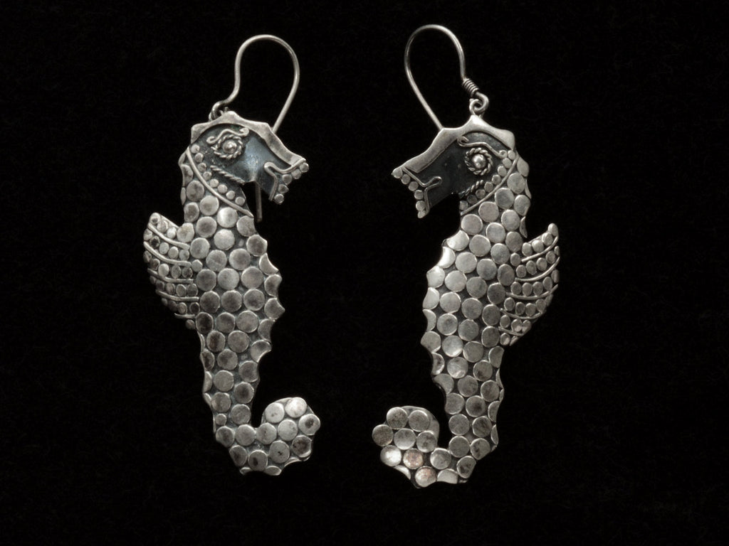 A pair of silver seahorse drop earrings textured with disks, shown against a plain black background.