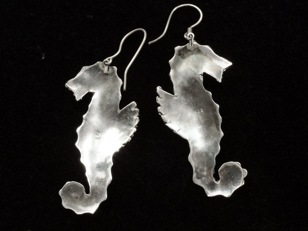Reverse sides of a pair of vintage silver seahorse earrings, on black background.
