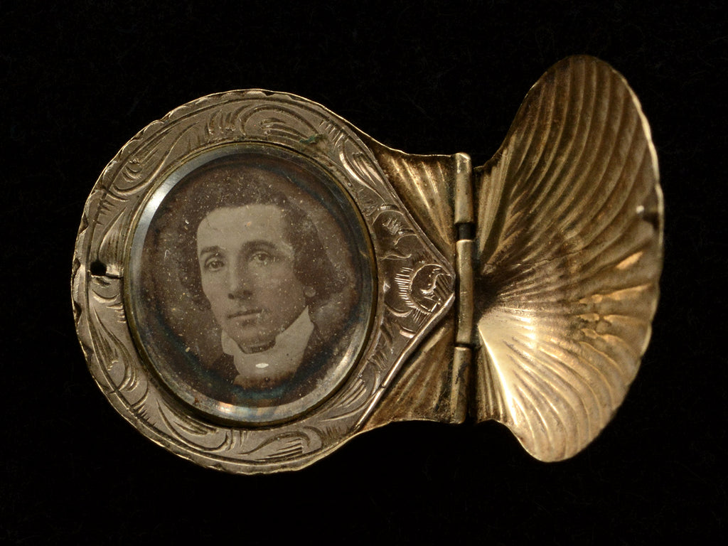 An antique Victorian scallop shell locket in gold, shown open with portrait of man inside, on black background