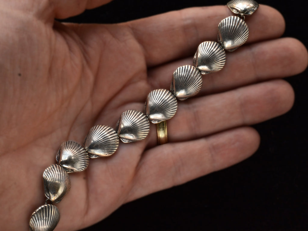 A silver bracelet with scallop shell links, on hand.