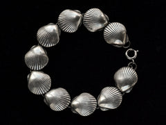thumbnail of A silver bracelet with scallop shell links, on black background.