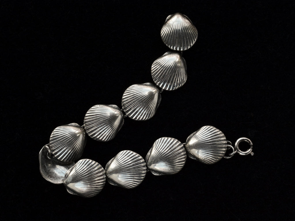 A silver bracelet with scallop shell links, laid out on black background.