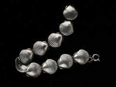 thumbnail of A silver bracelet with scallop shell links, laid out on black background.