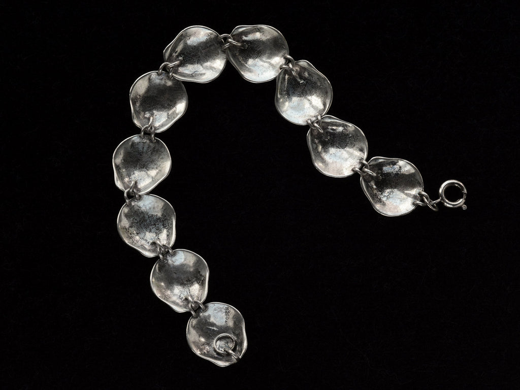 Reverse side of silver bracelet with scallop shell links, on black background.