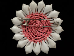 thumbnail of Reverse side of a vintage brooch featuring white shell petals arranged in a sunburst pattern around a central peach and brown shell cabochon, set in a pinkish-beige textured border, on black background. Shows safety pin fitting.