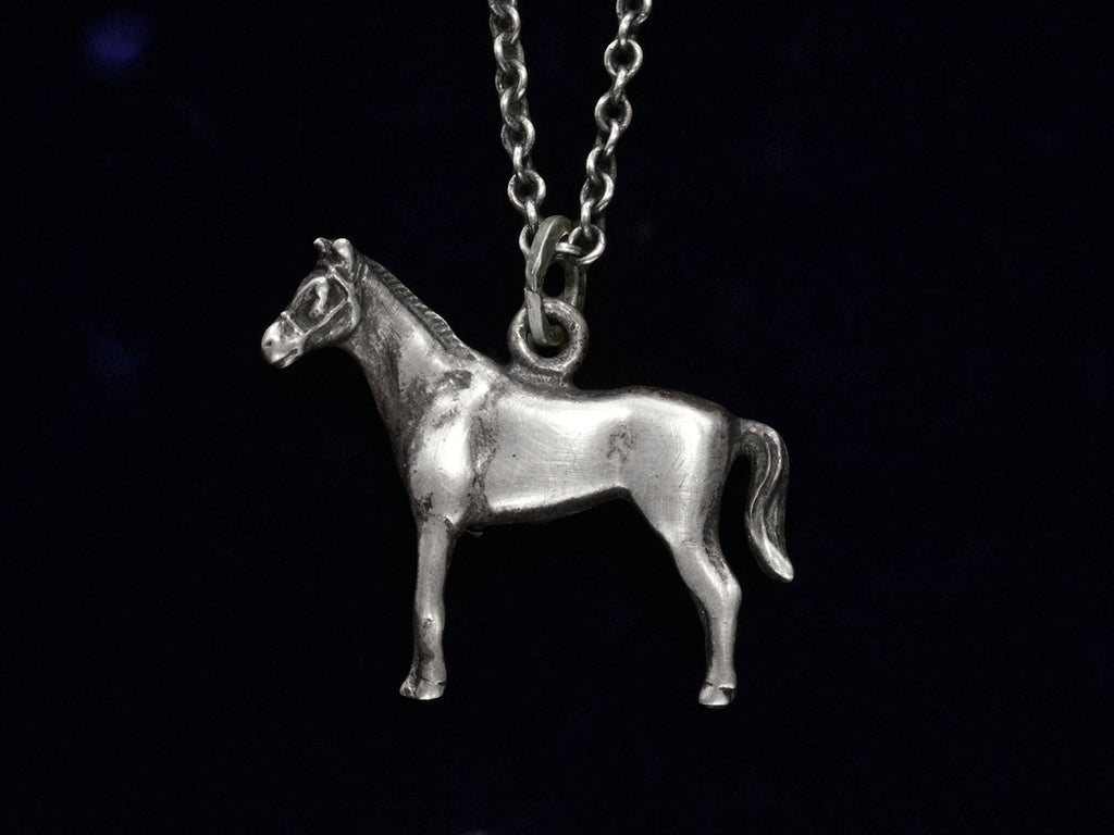 Silver horse pendant on a chain against a black background
