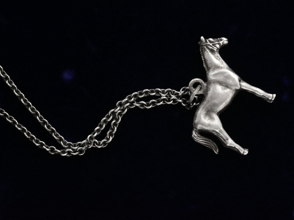 Opposite side of silver horse pendant on a chain against a black background