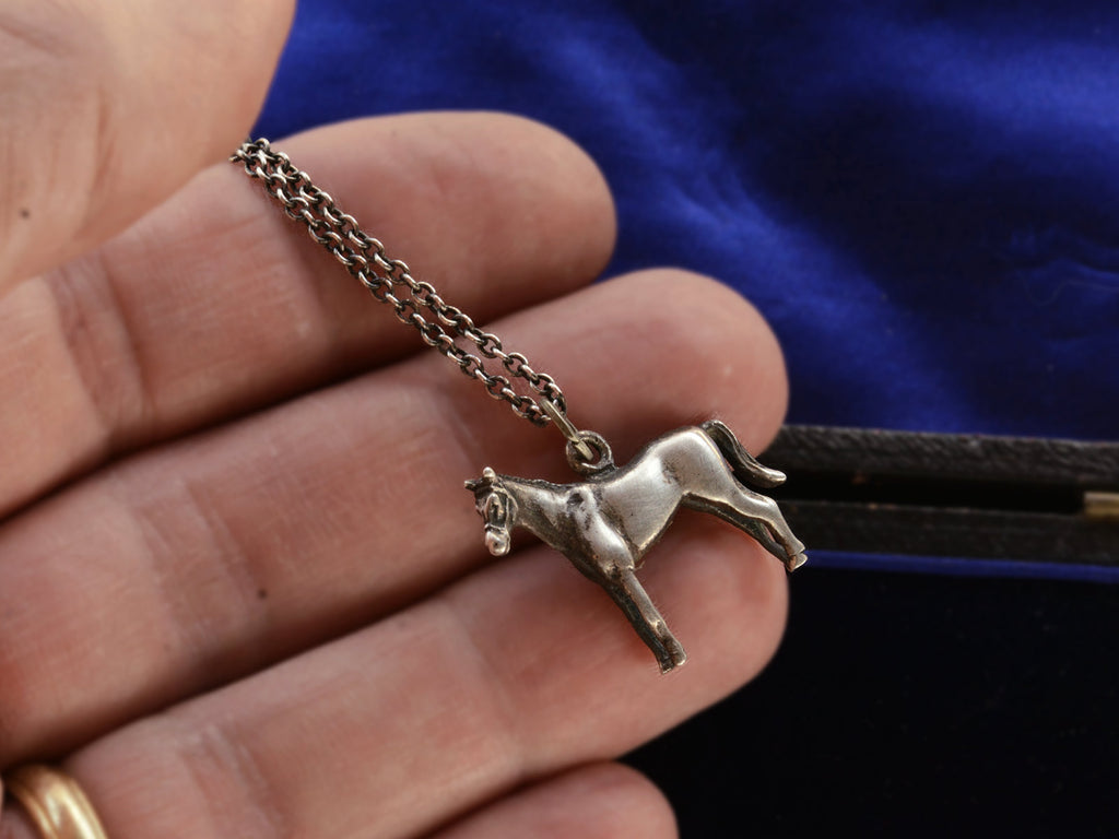 Silver horse pendant on a chain held in hand.