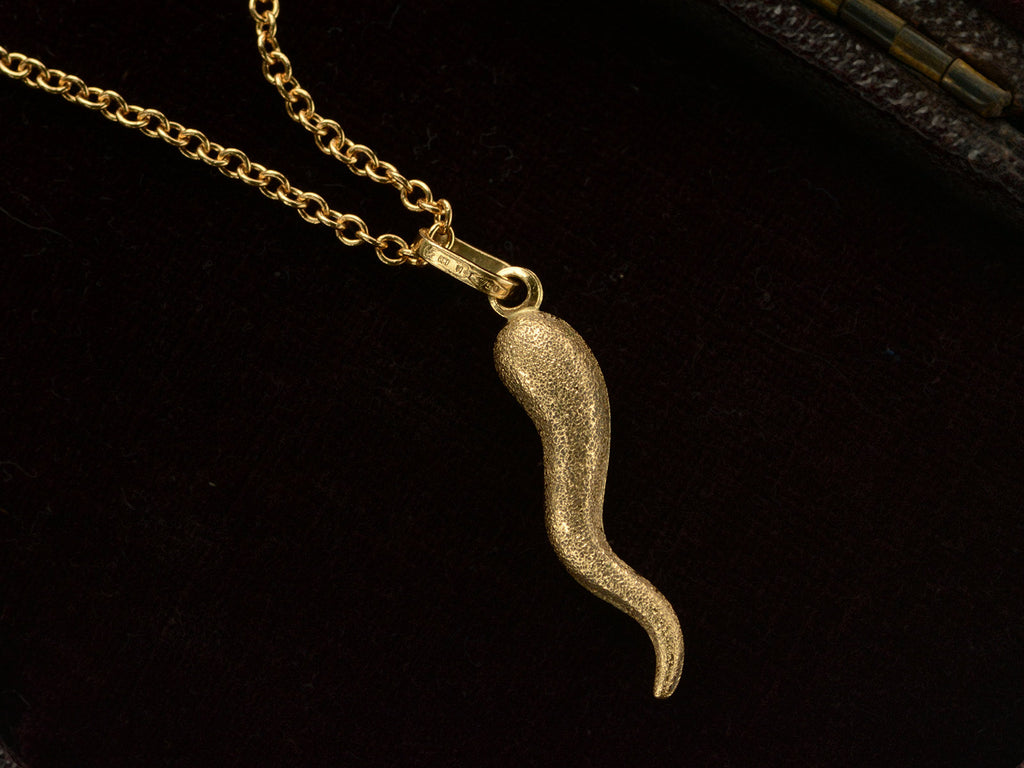 Vintage textured gold Italian cornicello charm on chain, with markings on the bale reading "860 VI 750". On black background.