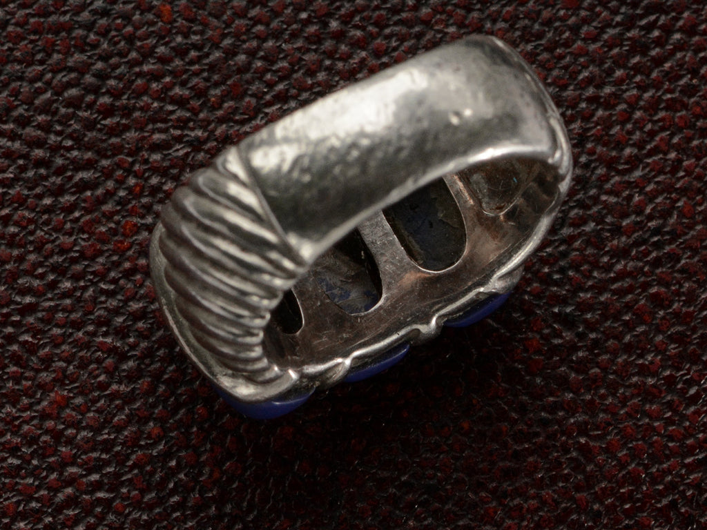 The inside of a silver ring featuring three polished dark blue resin stones, shown against dark textured background