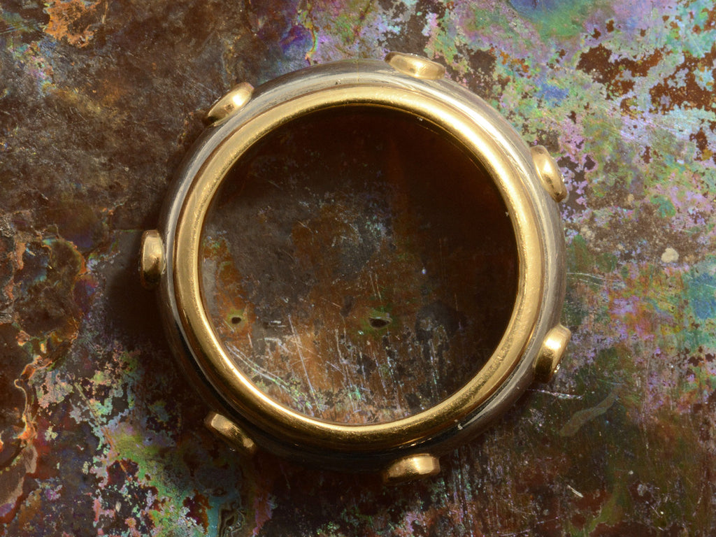 Side profile view of a vintage two-toned yellow and white gold diamond eternity band with a spinning mechanism. Shown on colorful background.