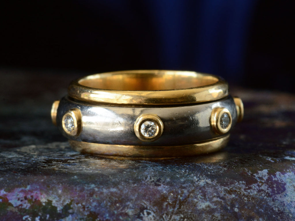 Front view of a vintage two-toned yellow and white gold diamond eternity band with a spinning mechanism. Shown on dark background.