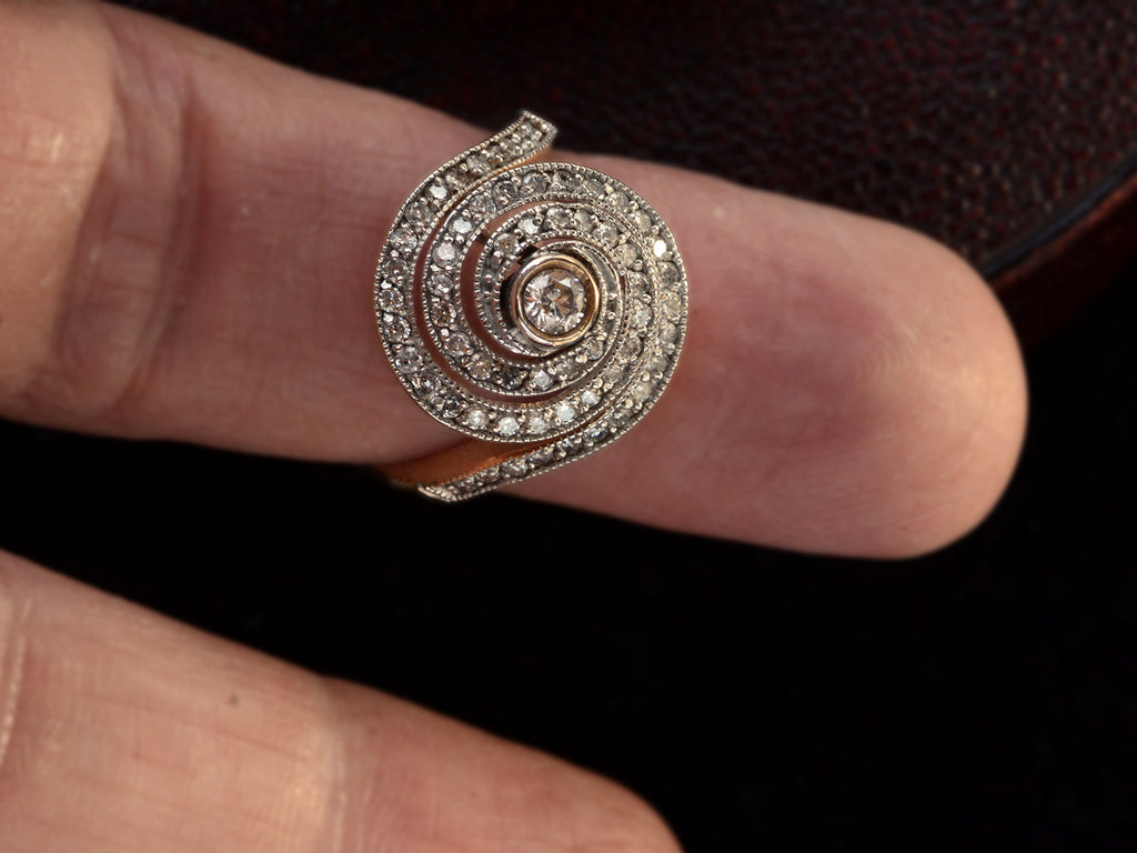 A vintage spiral form ring with diamonds in a white gold topped yellow gold mounting, shown on finger.