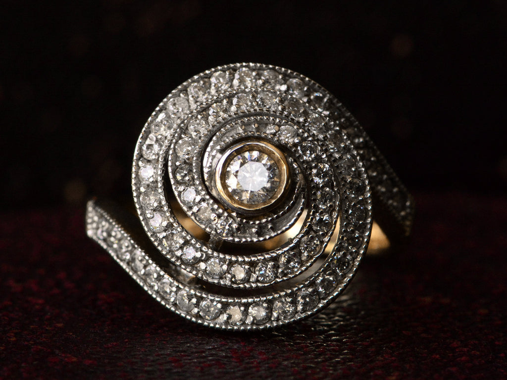 Face on view of a vintage spiral form ring with diamonds in a white gold topped yellow gold mounting, shown on dark background.