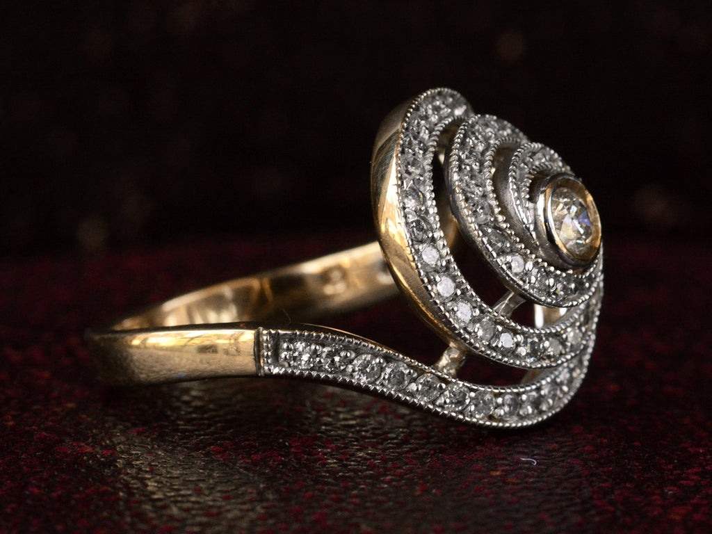 Left side view of a vintage spiral form ring with diamonds in a white gold topped yellow gold mounting, shown on dark background.