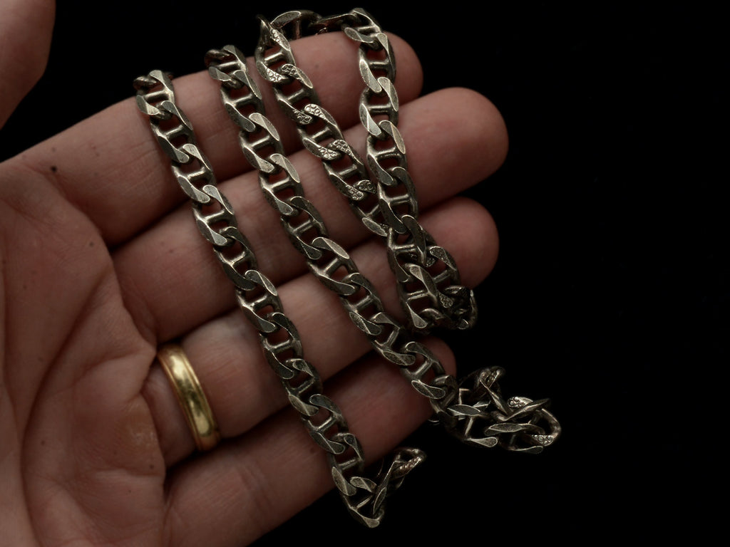 Close up of a hand holding a vintage sterling silver chain with beveled, flattened curb links, with texture on one side.
