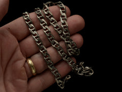 thumbnail of Close up of a hand holding a vintage sterling silver chain with beveled, flattened curb links, with texture on one side.