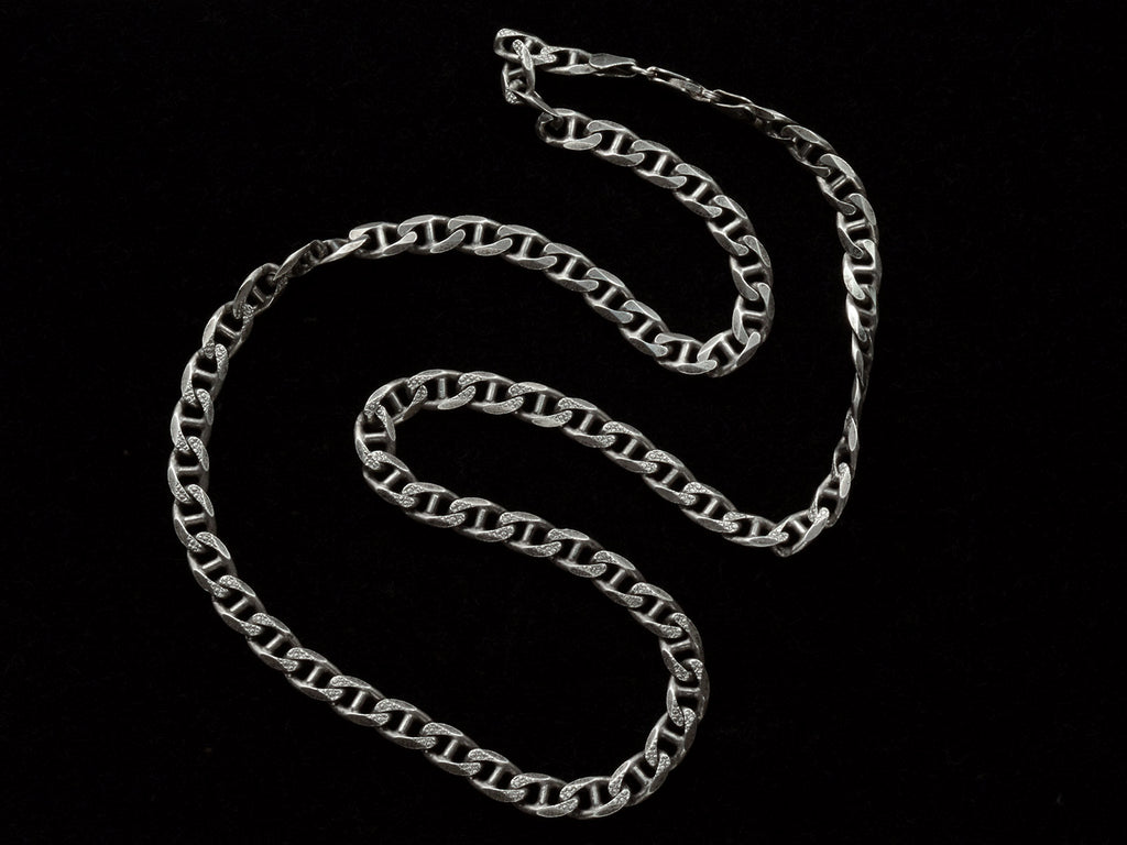 A vintage sterling silver chain with beveled, flattened curb links, with texture on one side, shown on black background.