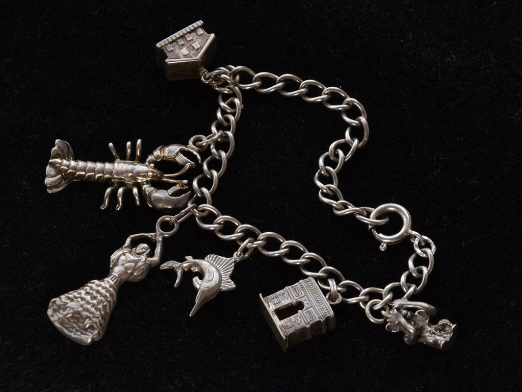 Vintage Silver Charm Bracelet showing a house, a lobster, a dancer, a fish, the Arc de Triomphe and a monkey. On a black background.