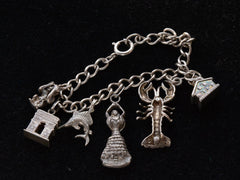 thumbnail of Reverse side detail of Vintage Silver Charm Bracelet showing a house, a lobster, a dancer, a fish, the Arc de Triomphe and a monkey. On a black background.