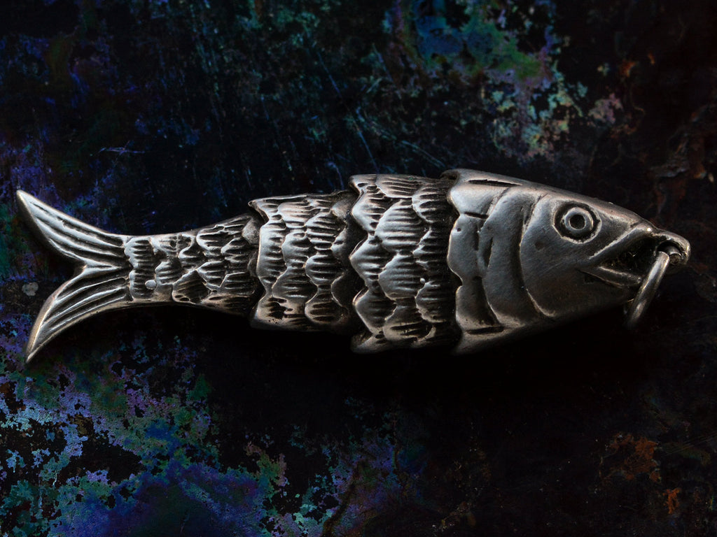 A right facing sterling silver articulated fish pendant on dark iridescent background.
