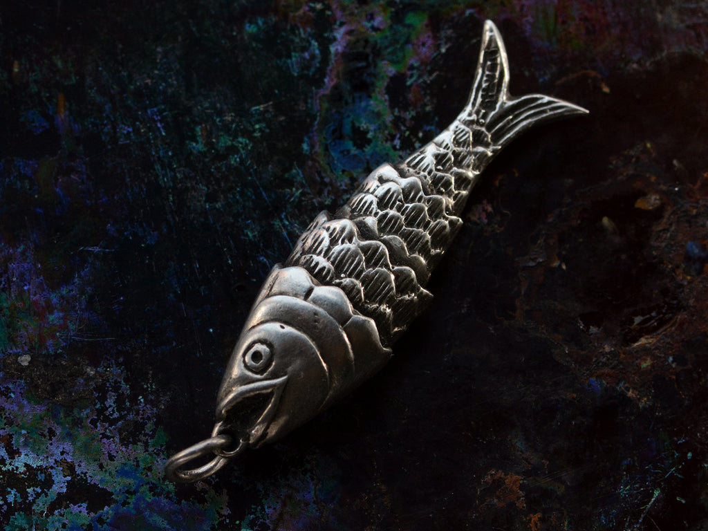 A down- facing sterling silver articulated fish pendant on dark iridescent background. "SILVER" stamp visible on tale.
