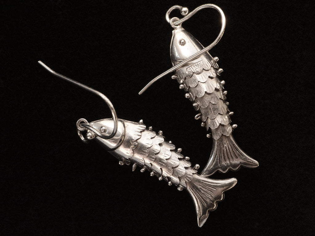 Reverse side of silver articulated fish earrings, on black background. "SILVER" stamp visible.