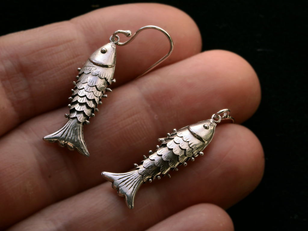 Silver articulated fish earrings, on hand. "SILVER" stamp visible.