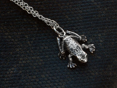 thumbnail of Detail of a vintage sterling silver frog pendant on chain, shown on dark textured background