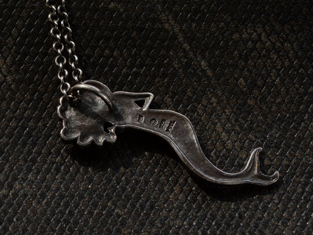 Reverse side of vintage silver mermaid pendant stamped with "925 and "PSCL", shown on dark textured background