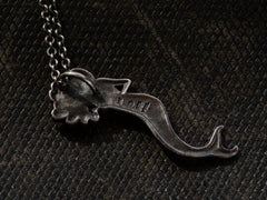 thumbnail of Reverse side of vintage silver mermaid pendant stamped with "925 and "PSCL", shown on dark textured background