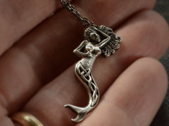thumbnail of Detail of vintage silver mermaid pendant with Celtic design on tail, shown hanging from cable chain on hand
