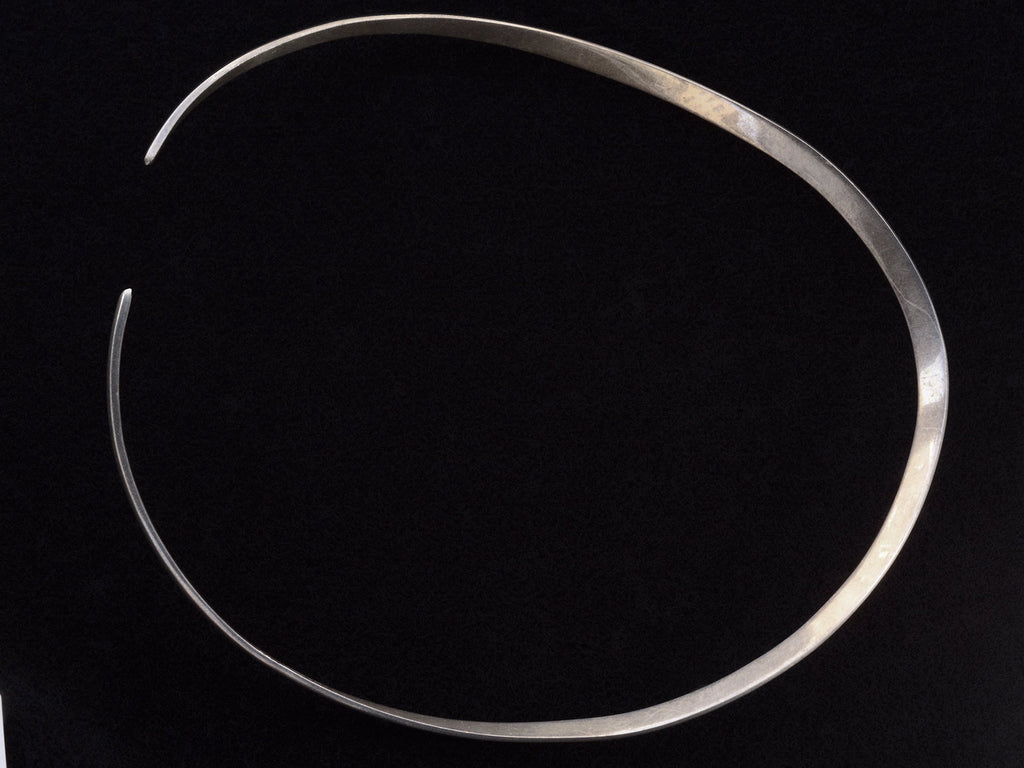 Reverse side of a simple silver neck cuff shown on black background.