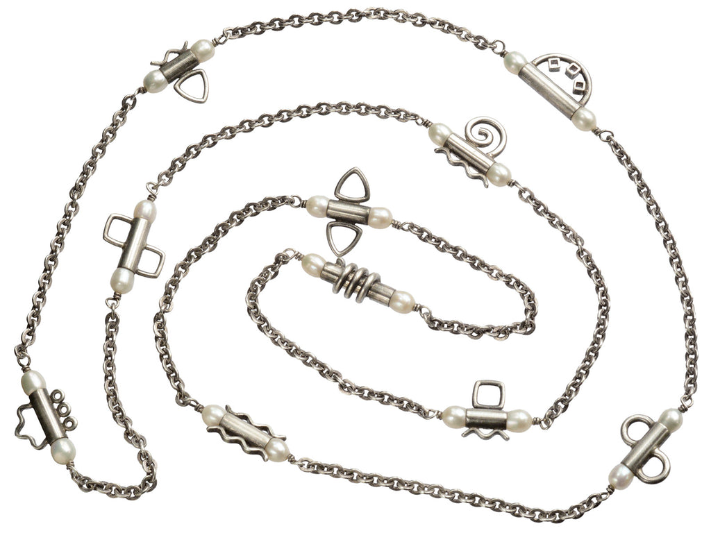 A c1990 long silver chain with interspersed tubular links, each decorated with pearls and a different geometric design or squiggle. Shown on white background.