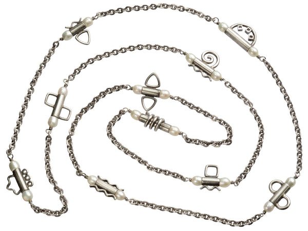 A c1990 long silver chain with interspersed tubular links, each decorated with pearls and a different geometric design or squiggle. Shown on white background.