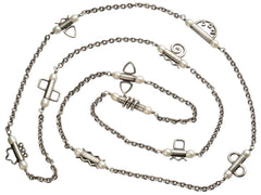 thumbnail of A c1990 long silver chain with interspersed tubular links, each decorated with pearls and a different geometric design or squiggle. Shown on white background.