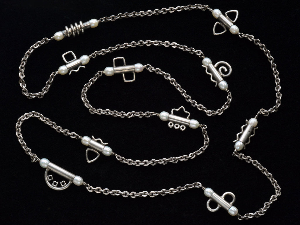 A c1990 long silver chain with interspersed tubular links, each decorated with pearls and a different geometric design or squiggle. Shown on black background.