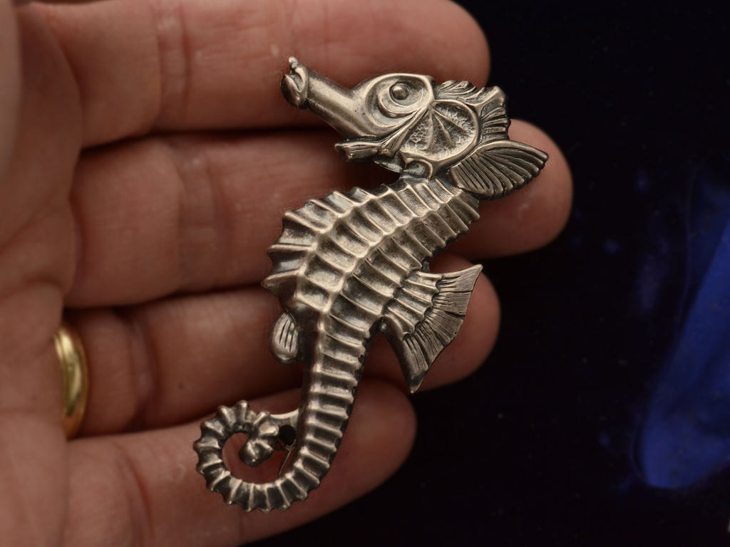 Front side of large vintage c1950 sterling silver seahorse brooch on hand.