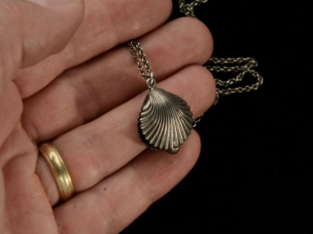 Antique silver shell pendant on a chain against held in hand.