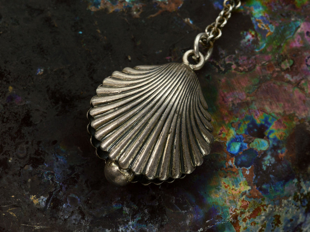 Detail of antique silver shell pendant on a chain against a dark colorful background.