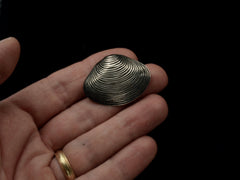 thumbnail of A silver ribbed clam shell brooch held in hand